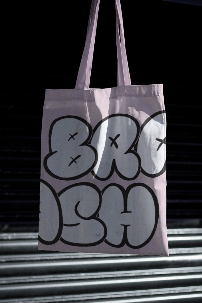 Tote bag mockup with bold graphic design hanging against metal shutters, ideal for showcasing urban style branding and typography.